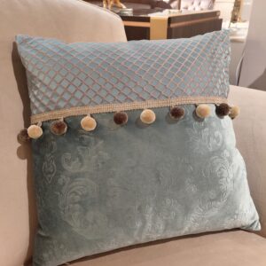 poduszka wykonana z najwyższej jakości welurowej tkaniny w odcieniu delikatnego błękitu, wpadającego w zieleń. Dodano także element z gładkiej tkaniny w kratkę. Dodatkowego uroku dodaje taśma z pomponami wszyta w poduszkę.
